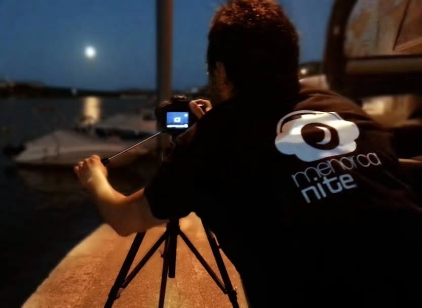Fotografía nocturna con cámara y trípode junto al mar, con la camiseta de Menorca Nite
