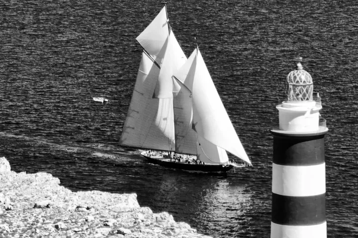 Velero clásico junto al faro de la entrada del puerto de Mahón, en blanco y negro · Aeroview.es