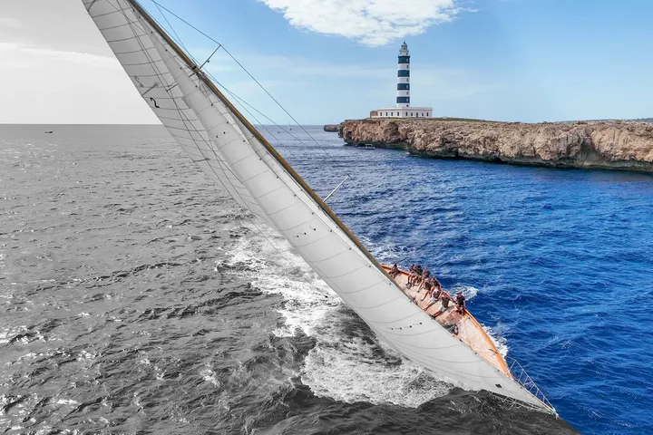 Embarcación de vela clásica navegando frente al faro del puerto de Mahón · Aeroview.es