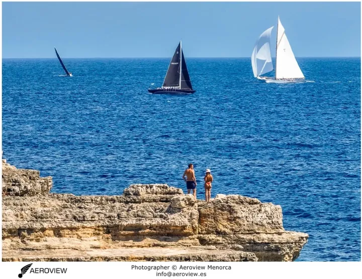 Público en el litoral observando la regata de vela clásica en Menorca · Aeroview.es
