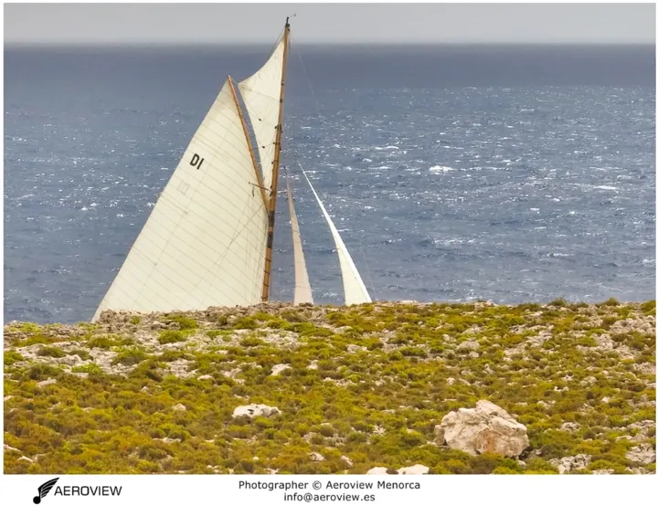 Velas de una embarcación clásica sobre la costa de Menorca · Aeroview.es